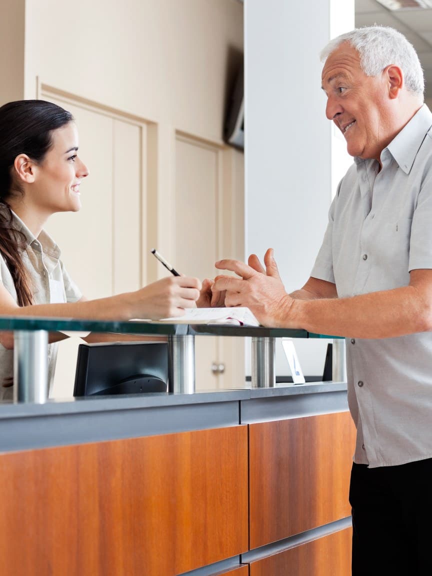 A receptionist at a front desk writing down a note for a visitor