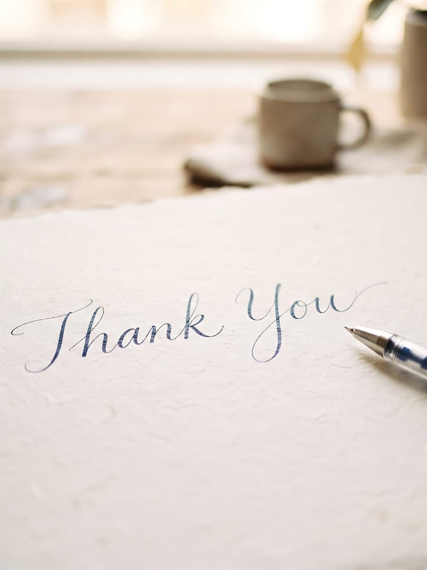 A thank-you card written in calligraphy, with a pen beside it
